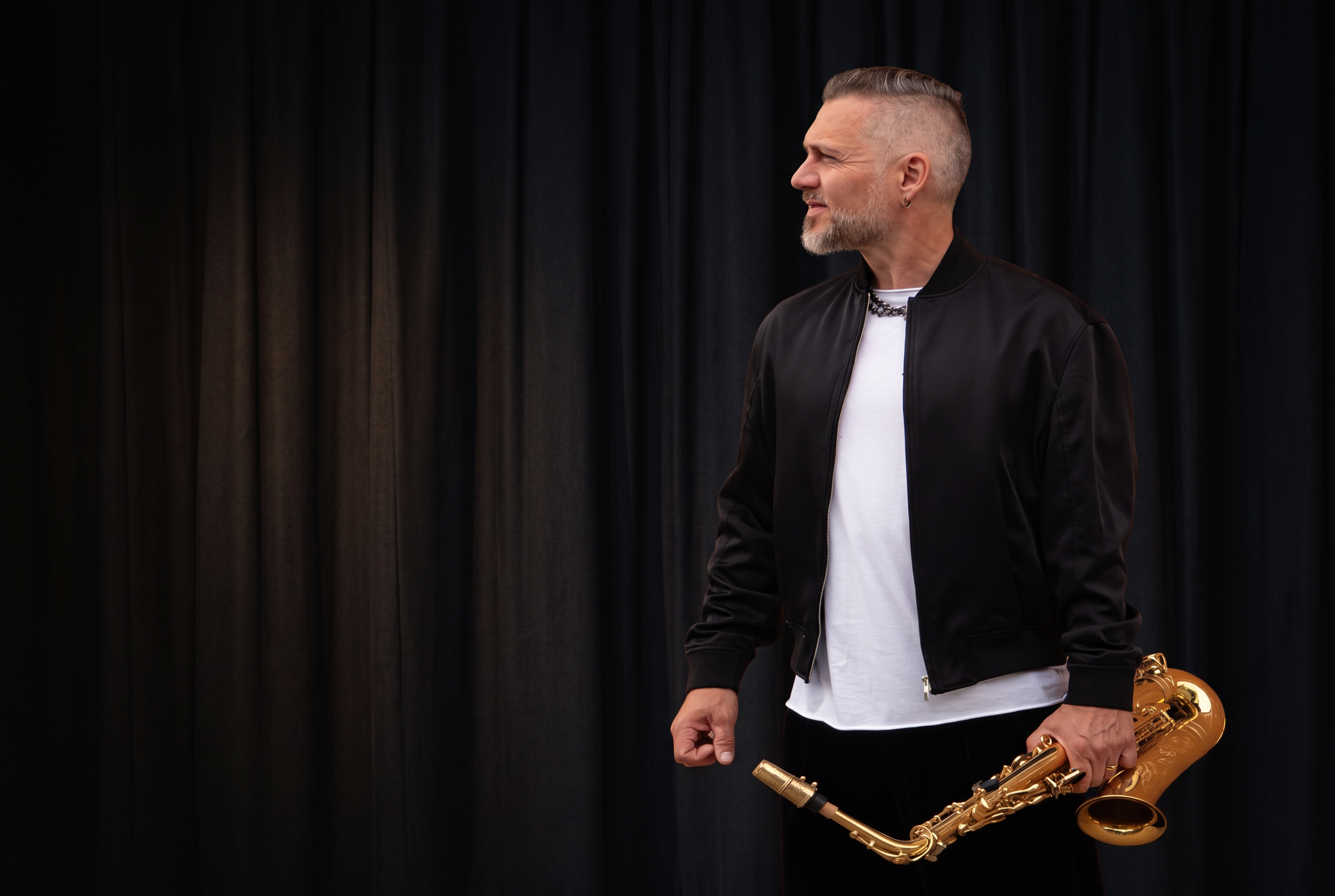Mattias Lejdal holding his saxophone against dark stage curtains